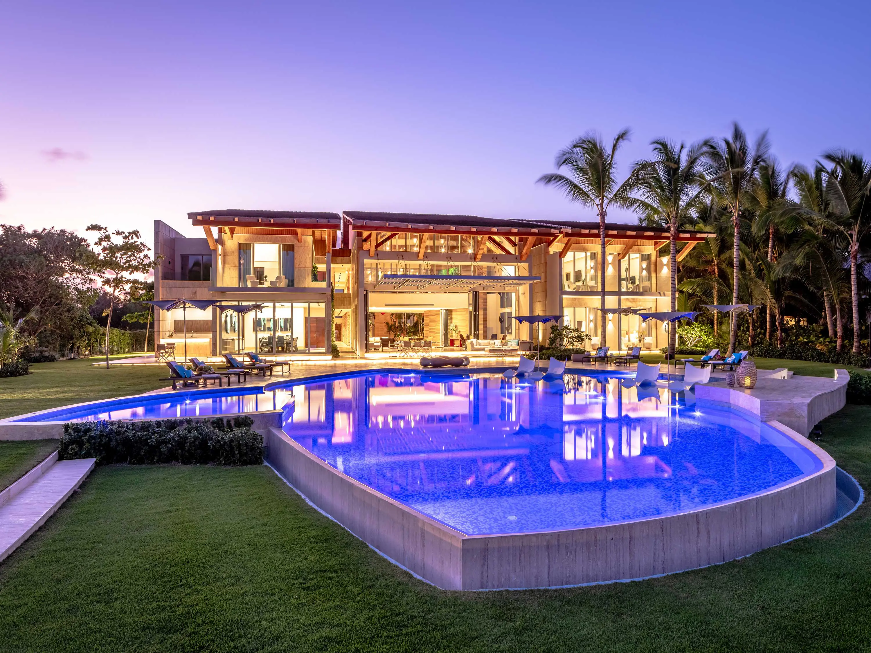 Purple sunset fading to light color, accentuating the pool's vibrant blue and in the background the beautiful villa.