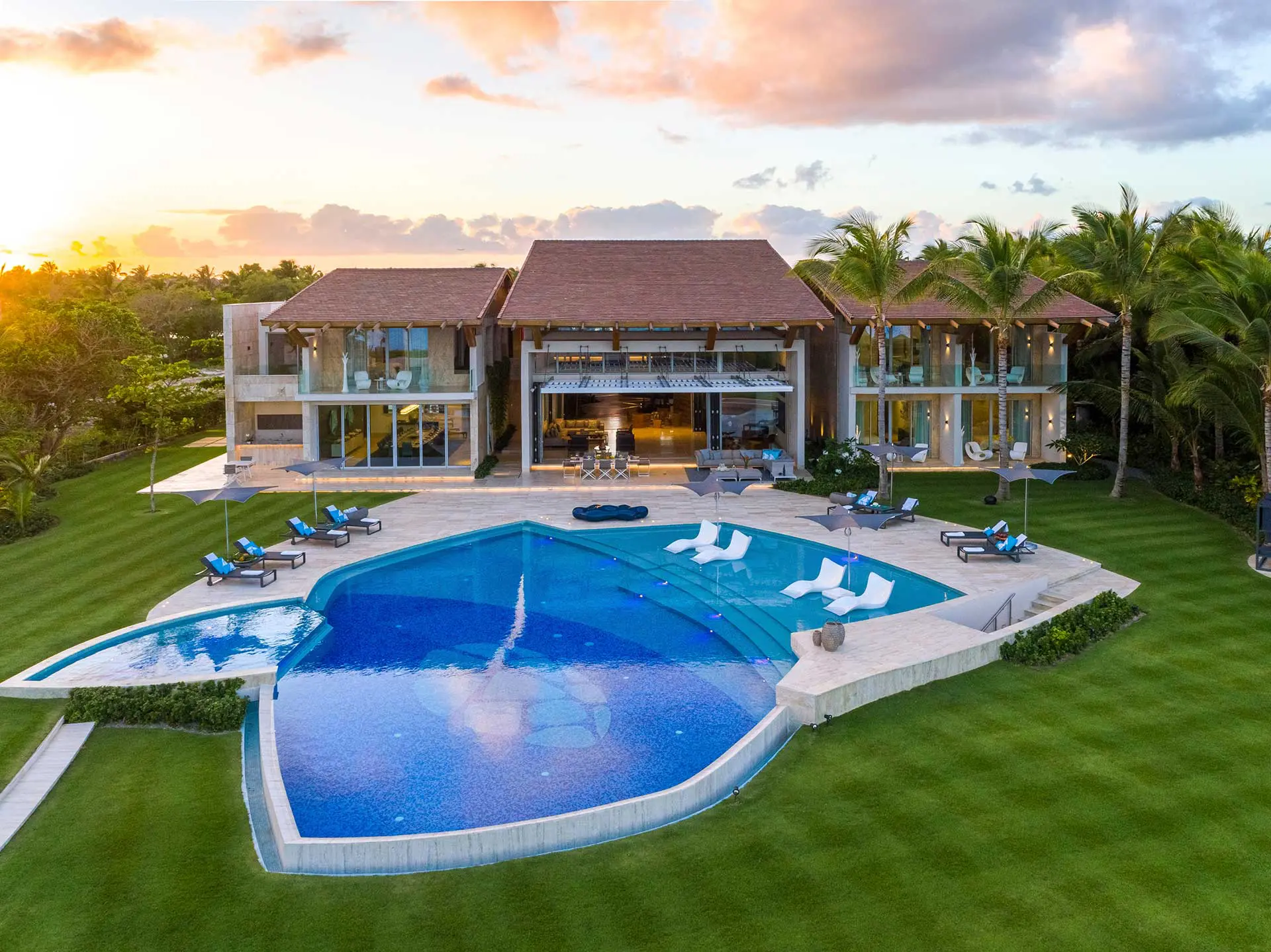 Orange sunset fading to light blue colors, accentuating the pool's vibrant blue and in the background the beautiful villa.